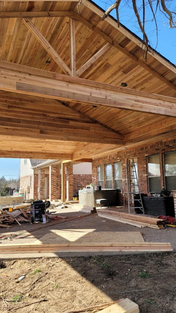 A large open porch with wood beams and a brick wall.
